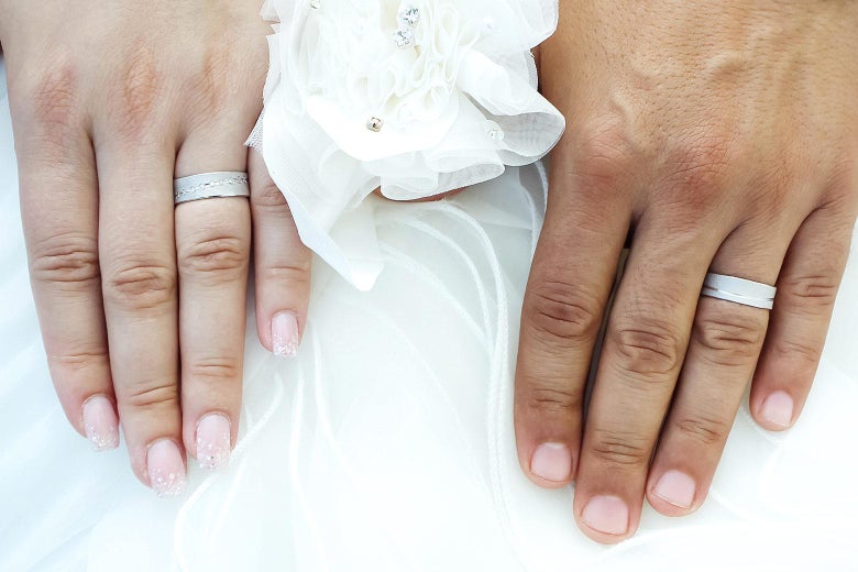 The wedding bands on a married couple flank a bow.